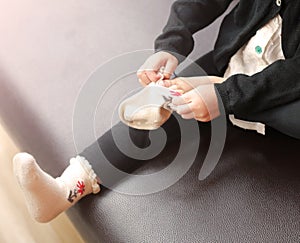 Little girl trying to put a socks on brown sofa