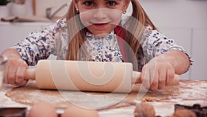 Little girl trying to stretch the dough with a rolling pin - close up