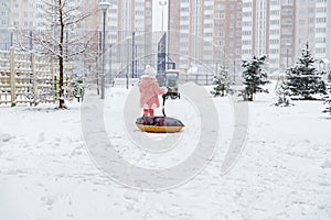 A little girl with a tubing went for a walk in the yard in the snow