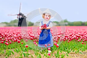 Little girl in tulips field with windmill in Dutch costume