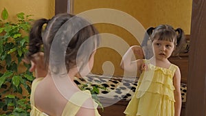 The little girl twists the tails in front of the mirror. A beautiful girl with tails on her head looks at the owl reflection. A ch