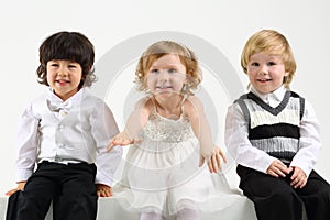 Little girl and two boys sit on white big cubes on