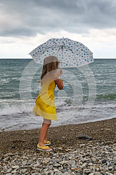 Little girl with umbrella on beach in bad weather