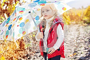 Little girl with umbrella in red vest outdoor