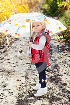 Little girl with umbrella in red vest outdoor