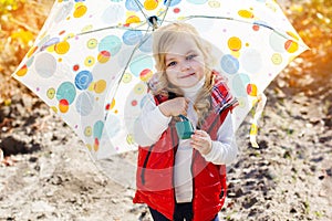 Little girl with umbrella in red vest outdoor