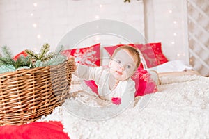 A little girl under one year old in an airy dress on a large bed in a room decorated for Christmas