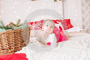 A little girl under one year old in an airy dress on a large bed in a room decorated for Christmas