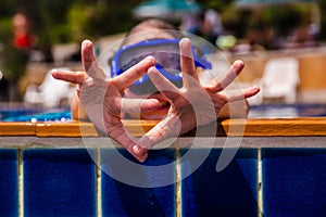 Little girl in underwater mask show hands with wrinkles fingers after playing in the swimming pool, close-up portrait