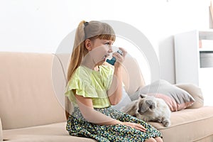 Little girl using asthma inhaler near cat at home