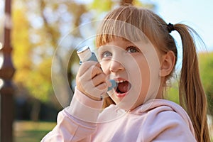 Little girl using asthma inhaler outdoors