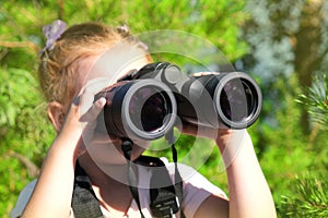Little girl using binoculars in the forest. Exploring the world. Outdoor activities
