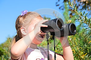 Little girl using binoculars in the forest. Exploring the world. Outdoor activities