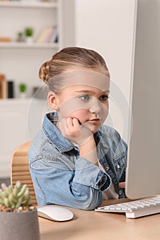 Little girl using computer at table in room. Internet addiction