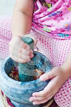 A little girl is using the mortar and pestle or lesung batu in Malay.