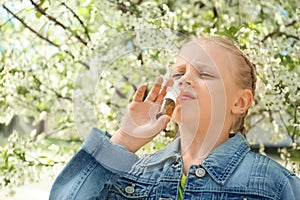 Little girl using nasal drops near blooming tree. Allergy concept