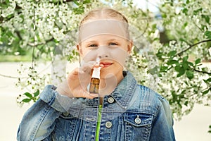 Little girl using nasal drops near blooming tree. Allergy concept