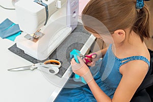 Little girl using a sewing machine to sew on a piece of fabric. Creative tailoring workshops for children