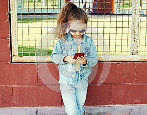 Little girl using smartphone, stylish child wearing a jeans clotes