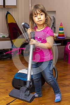 A little girl vacuums the room, puts things in order.  Cleaning in the apartment.