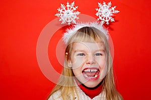 The little girl is very emotionally angry and expresses dissatisfaction. Red background. Portrait. Christmas decoration