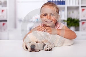 Little girl at the veterinary doctor with her puppy dog asleep on the examination table
