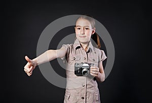 Little girl with vintage camera thumb up at black background