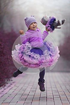Little girl in the violet dress dancing with a toy cat