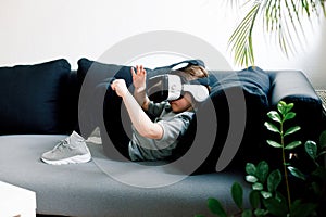 Little girl with virtual reality headset lying on sofa at home