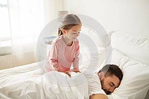 Little girl waking her sleeping father up in bed