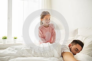 Little girl waking her sleeping father up in bed