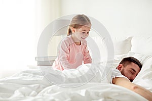 Little girl waking her sleeping father up in bed