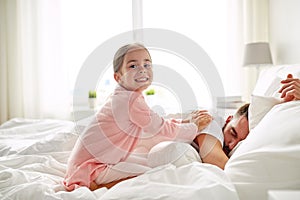 Little girl waking her sleeping father up in bed