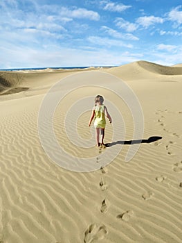 A little girl walk and leaves footprints on desert sand dune