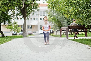 A little girl is walking with a backpack down the street. The concept of school, study, education, friendship, childhood.