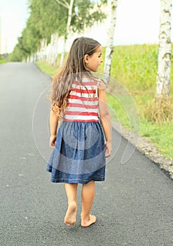 Little girl walking barefoot on asphalt street