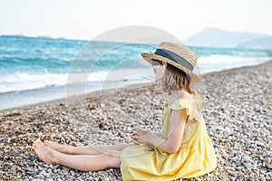 Little girl walking on beach, sea ocean shore in romantic yellow dress, straw hat. Playing in sand, blue waves. Family