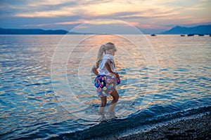 Little girl walking on beautiful ocean beach. Happy preschool child play by sunset on sea beach. Family vacations with