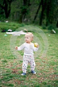 Little girl walking in a green meadow with an apple in her hand