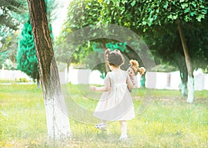 A little girl walking in green park in a white dress with a doll