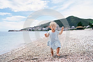 Little girl walking on a pebble beach with a pebble in her hand