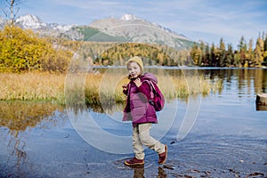 Little girl walking in the shore of lake, in the middle of beautiful autumn nature.