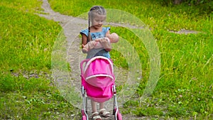 Little girl with walking with stroller and baby doll in park
