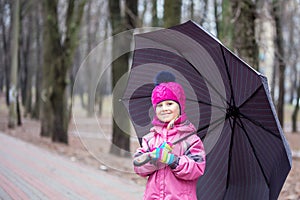 Little girl walking under umbrella in a city park