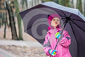 Little girl walking under umbrella in a city park