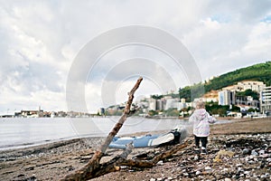 Little girl walks along the beach towards an inflatable boat. Back view