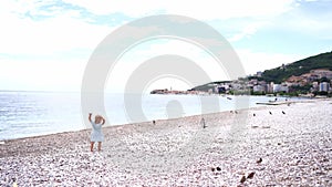 Little girl walks along the pebble beach to the sitting birds