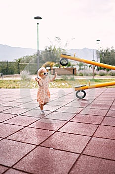 Little girl walks along the rubber surface of the playground to the swing-balancer