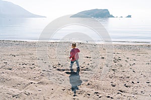 Little girl walks along the sandy beach near the sea. Back view