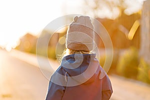 Little girl walks along a sunny road. Back view